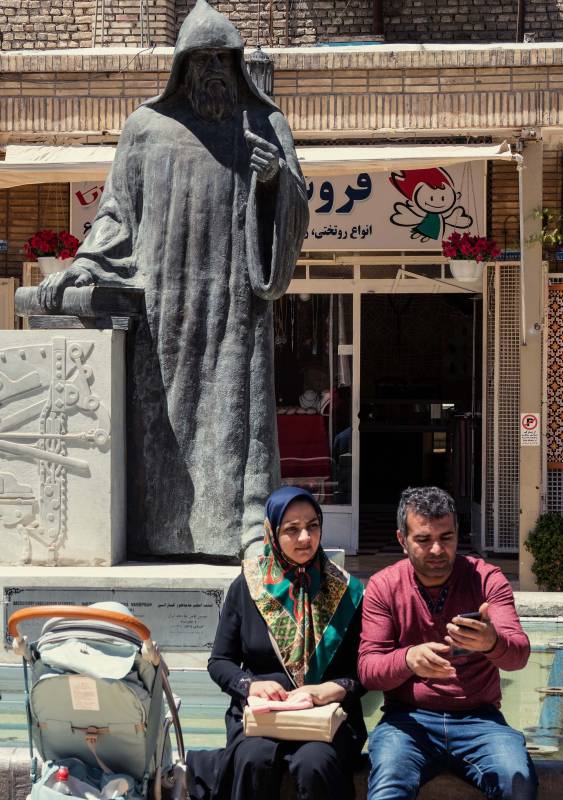2019, Isfahan, Statue des armenischen Erzbischof Khachatour Kesaratsi vor der Vank-Kathedrale. Er gründete 1636 das erste Verlagshaus in Persien (Iran) und im Nahen Osten und druckte das erste Buch in Persien: Saghmosaran (der Psalter auf Armenisch).  Die Statue zeigt den Erzbischof mit dem Relief einer Druckmaschine und hält in der einen Hand Bücher und in der anderen den Stempel eines Buchstabens, der im Hochdruckverfahren verwendet wurde. Vorne Ehepaar mit heutiger Handy-Kommunikation.