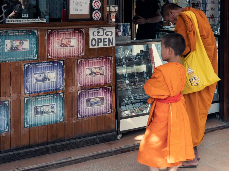 2019, junger Mönch in Luang Prabang vor einer Wechselstube.
